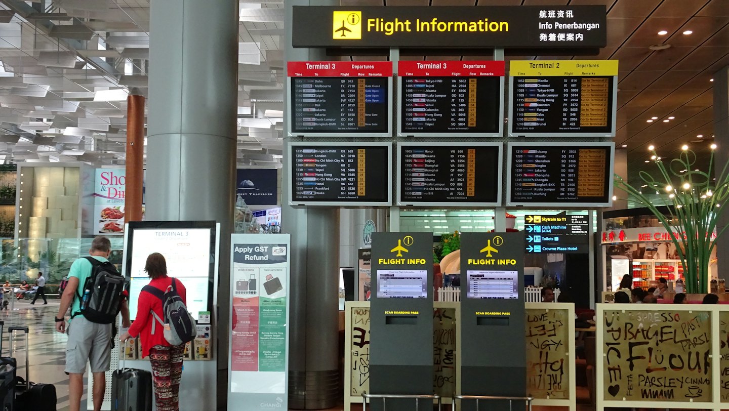 Two travelers check flight information on a digital airport kiosk.