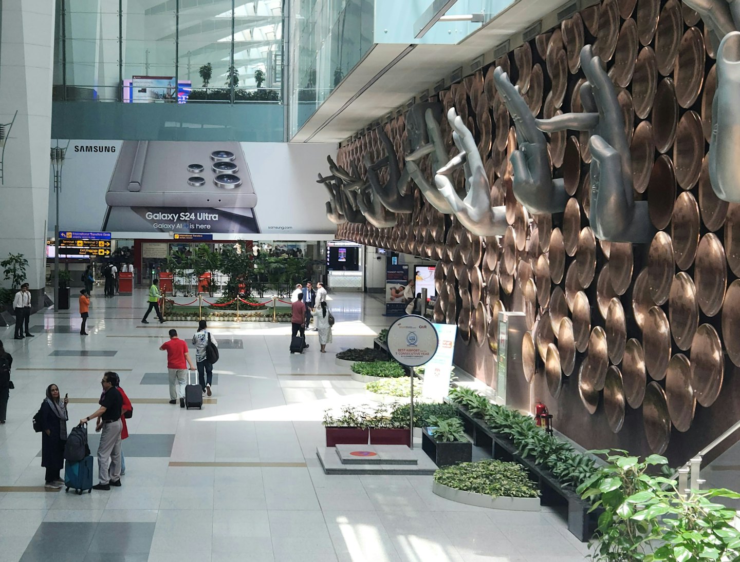 Travelers with luggage in a modern airport terminal with a Samsung ad.